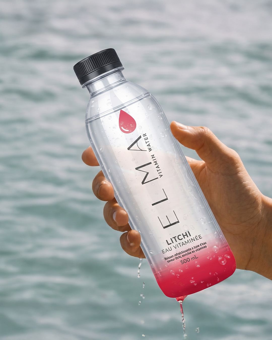 Bottiglia ELMA gusto litchi tenuta davanti al mare